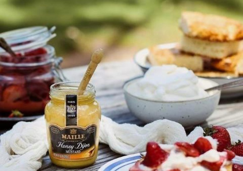 Tarta de mostaza a la miel, fresas maceradas y nata. Sobre mesa de madera al aire libre rodeada de cuencos con los ingredientes 